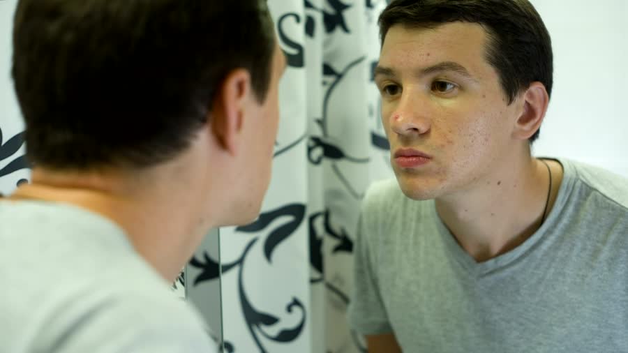 A man looking closely at his skin in the bathroom mirror