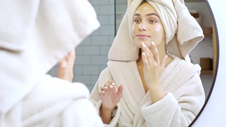 A woman in a bathrobe checking her skin in a round mirror